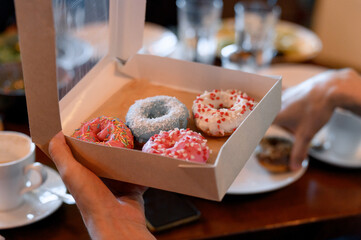 A hand holds a box with four colorful glazed donuts
