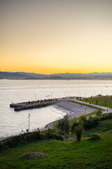 Obraz premium A high-angle view of the Explanada de Gamazo waterfront promenade in Santander, Spain, during a beautiful golden hour sunset over the bay and mountains.