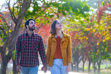 Happy caucasian couple walking together in the public park during autumn with maple and beech tree for fall color travel destination and family happiness
