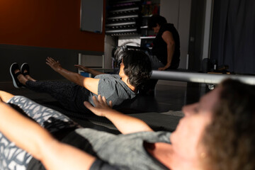An older woman performs a Pilates exercise with her legs, called the hundred, in a small gym, alongside other women