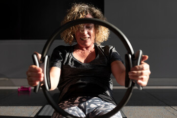 A middle-aged woman, senior, performing a Pilates exercise with a hoop in her hands
