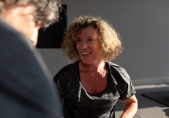 A senior woman smiles contentedly and talks to the instructor after a Pilates exercise in a small gym in her town