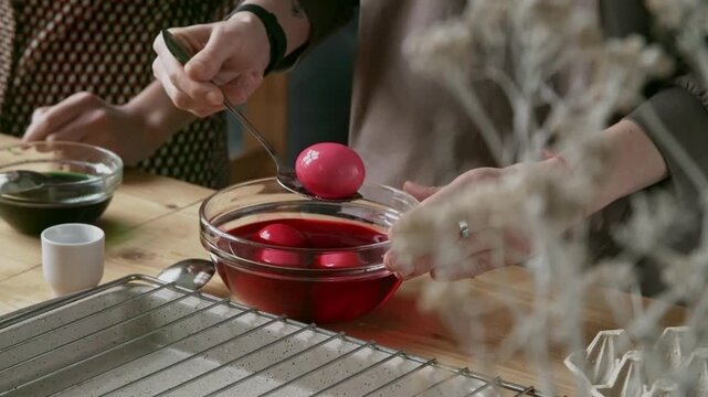 Mid-section shot of unrecognizable woman taking out painted hardboiled eggs from bowl with organic red dye and putting them on tray to dry out