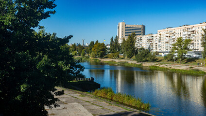 Kyiv urban landscape showcasing the Rusanivka Canal, integrating residential apartment buildings with lush green space, a tranquil public park, and the city skyline under a clear blue sky