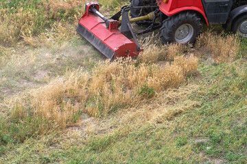 Weeding with a lawnmower attached to a tractor on an overgrown field or lawn area, work of a large lawnmower cutting weeds, tractor work with a lawnmower.