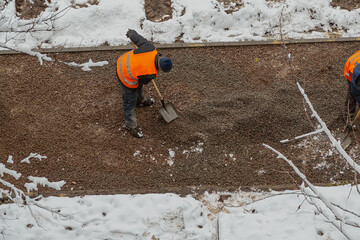 A worker is using a shovel on a gravel road during bad weather, municipal services are carrying out road landscaping.