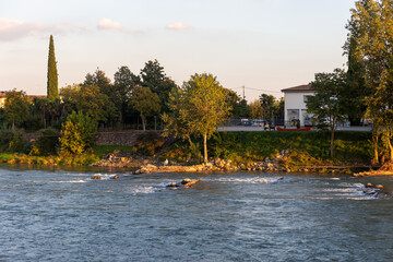 A scenic landscape capturing a moment of leisure and relaxation. A fisherman sits on the rocks while others chat, embodying a tranquil, slow-paced lifestyle.