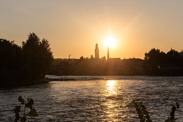 A classic European sunset scene. The skyline of a charming village, with its bell tower and bridge, is cast in shadow by the brilliant setting sun.