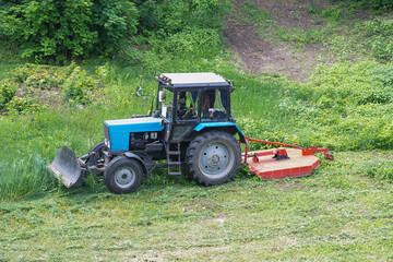 A tractor on a green field during the removal of weeds and overgrown grass, weed removal from a green field, agricultural work in summer.