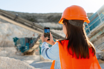 Female construction worker holding mobile phone taking photo at quarry site