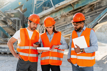 Croup of multinational workers having discussion at worksite near heavy machinery