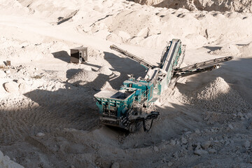 Industrial rock crusher working at limestone quarry surrounded by rocks and gravel
