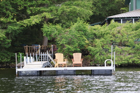A view of an peaceful lakeside dock with Adirondack chairs.