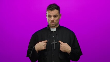 Hispanic man in black clergy attire standing isolated against pink background, expressing denial with hand gestures.