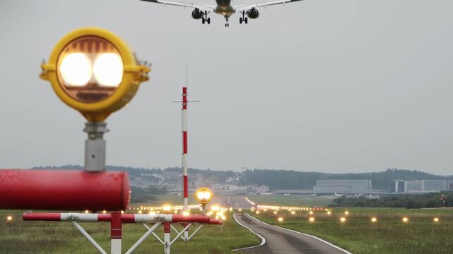 Commercial passenger airplane landing on an illuminated airport runway strip. Ground level, rear of the plane, very low altitude, telephoto, cloudy sky, real time footage