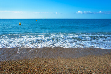 Sunny beach in Barcelona by the blue sea and gentle waves rolling on the pebbly shore