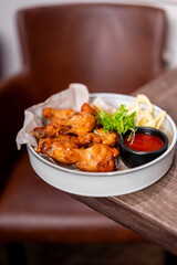 Plate of fried chicken wings with fries, dipping sauce, and lettuce garnish on parchment-lined white plate, served on wooden table in cozy restaurant setting.