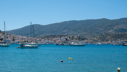 Poros Island harbor Greece. Boats on calm blue water, traditional architecture hillside houses and summer sky
