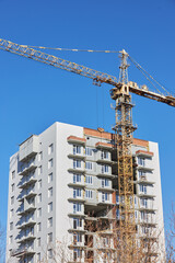 Building construction is underway with a large crane towering over a new multi-story structure. Clear blue skies serve as a backdrop to this active site where workers are busy