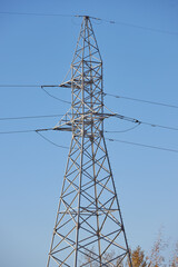 tall steel power tower rises against a bright blue sky in an open area. structure is surrounded by trees, showcasing the utility of electricity in rural regions