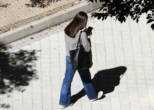 Chica nomof&oacute;bica adicta al tel&eacute;fono mirando el m&oacute;vil y andando sin levantar la vista del suelo