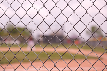 Chain link fence in focus with a baseball field in the blurry background