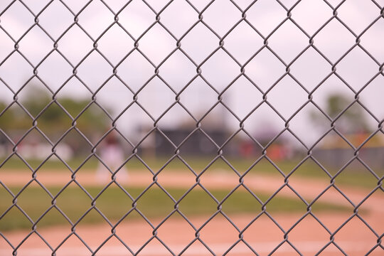 Chain link fence in focus with a baseball field in the blurry background
