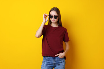 Woman wearing stylish burgundy t-shirt and sunglasses on yellow background