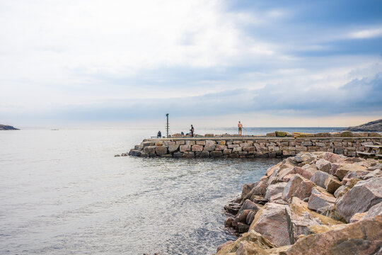 People standing on rocky jetty beside ocean.