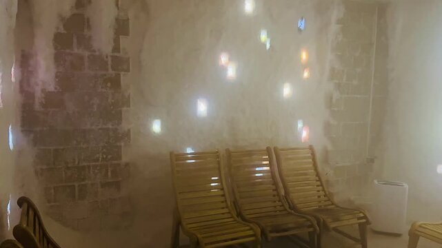 Mesmerizing colorful light patterns moving across the salt covered walls of a therapeutic cave, illuminating the empty wooden lounge chairs during a relaxing halotherapy session at a wellness spa