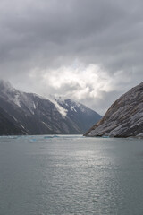 The Sun peeking through overcast weather over the foggy mountains over the ice-cold waters in Alaska