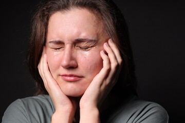 Fototapeta premium Sad young woman crying on black background