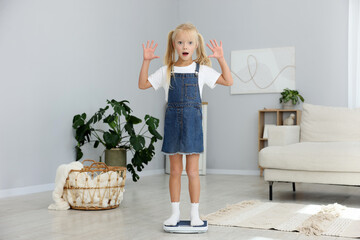 Little girl measuring her weight on scales at home