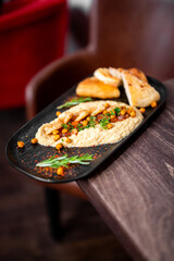 Middle Eastern hummus with roasted chickpeas, parsley, spices, and pita bread served on a black plate over rustic wooden table in cozy restaurant setting.