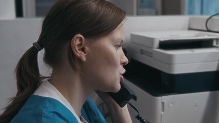Close-up view of Caucasian female healthcare operator talking on phone rescheduling patients appointment during workday in diagnostic centre