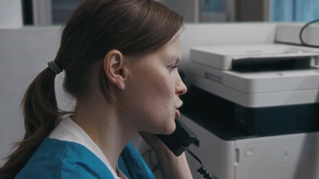 Close-up view of Caucasian female healthcare operator talking on phone rescheduling patients appointment during workday in diagnostic centre