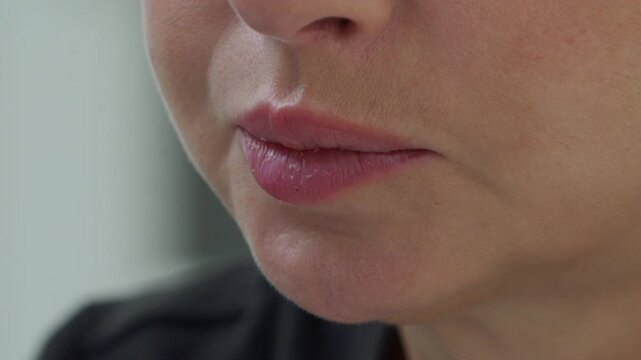 A close-up view focuses on a woman's mouth as she actively chews and enjoys a sandwich, capturing the motion and texture of eating.