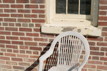 old weathered plastic lawn chair by a brick wall with window outdoors