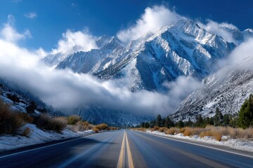 Mountain road surrounded by snow-capped peaks and clouds on a clear day in early morning light