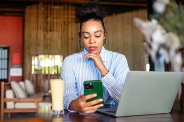African american woman with a phone and laptop in a cozy space feeling unengaged while waiting