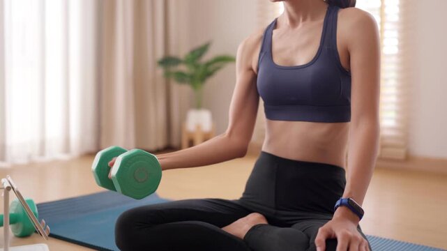 Asian adult woman perform strength training dumbbell home workout following online fitness program for healthy lifestyle