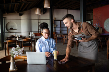 Collaborative cafe moment with waiter and businesswoman, freelancer using tech while working