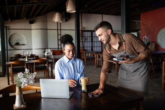 Collaborative cafe moment with waiter and businesswoman, freelancer using tech while working