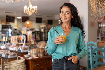 Confident woman with long black hair wearing a turquoise cardigan and black jeans, standing in a...