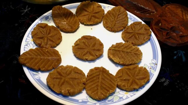 Beautifully shaped uncooked Thekua arranged on a plate in an Indian kitchen. The Thekuas are crafted in flower and leaf patterns, prepared for Chhath Puja. 