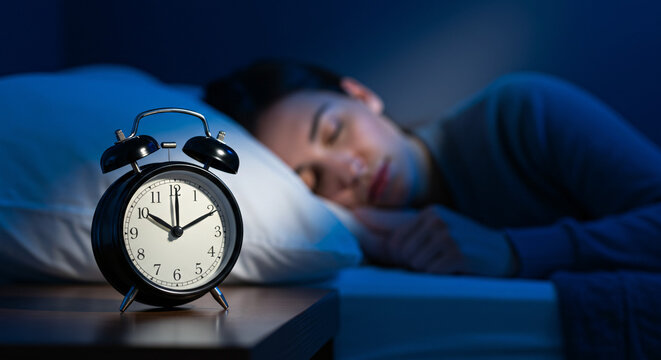 Man peacefully sleeping next to alarm clock in dimly lit bedroom, concept of Daylight Saving Time Change  