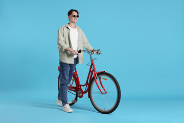 Fototapeta premium Handsome man with red bicycle on light blue background