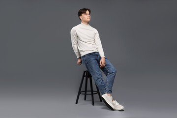Man in stylish jeans on stool against grey background