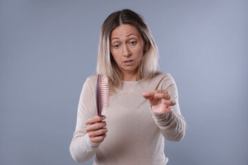 Alopecia problem. Worried woman taking her lost hair from brush on grey background
