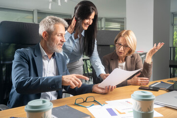 Three busy happy middle aged professional business man and two women executive leaders team using laptop working on computer at work desk having conversation on financial project at meeting in office.